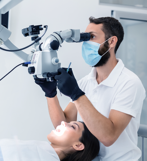 Un dentista che indossa maschera e guanti usa un microscopio per esaminare la bocca di una bambina. La bambina è sdraiata su una poltrona odontoiatrica con la bocca aperta sotto una luce luminosa per l'esame, evidenziando la delicatezza delle cure specialistiche per i bambini dentisti.