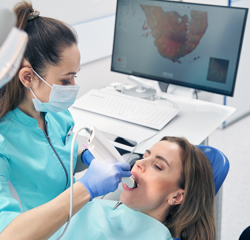 Dental children Milano con un dentista utilizza un dispositivo di scansione portatile per esaminare la bocca di una paziente. Il paziente è seduto sulla poltrona e la scansione dentale è visibile sullo schermo del computer: una tecnologia ideale sia per gli adulti che per i bambini.