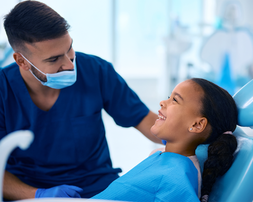 Estrazione dente da latte eseguita da un dentista seduto accanto a una bambina sulla poltrona odontoiatrica che sorride, in uno studio dentistico luminoso