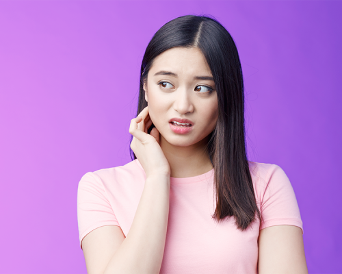Trauma dentale Ricostruzione dentale rappresentato da una ragazza con espressione preoccupata che si tocca la guancia con una mano, indossando una maglietta rosa su sfondo viola uniforme.