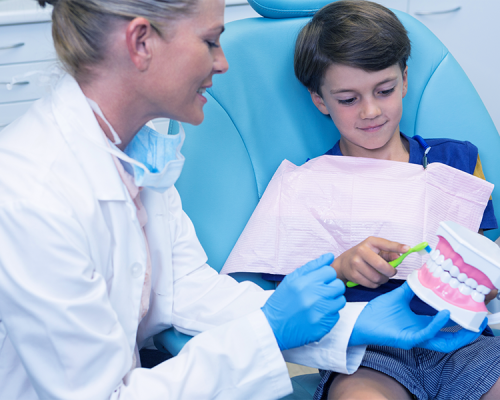 Igiene orale bambini rappresentata da un dentista che mostra a un bambino come spazzolare correttamente i denti utilizzando un modello dentale, per aiutarlo a imparare una routine di pulizia efficace e divertente.