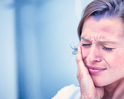 Byte per bruxismo mostra una donna che si tocca la guancia con espressione dolorante indicando possibile dolore dell’articolazione temporo-mandibolare