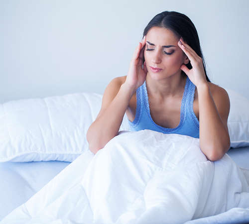 Byte per bruxismo evidenzia una donna seduta sul letto che si massaggia le tempie mostrando mal di testa mattutino legato al serramento notturno