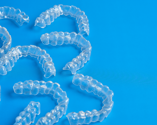 Byte per bruxismo presenta diverse mascherine trasparenti dentali disposte su sfondo blu per rappresentare i dispositivi personalizzati