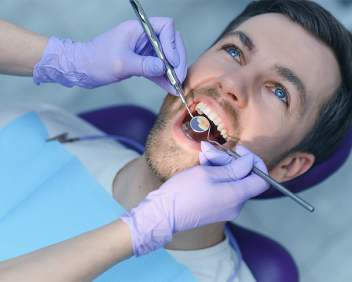 Otturazioni dentali mostra un paziente adulto durante un controllo odontoiatrico mentre il dentista utilizza specillo e specchietto per verificare la presenza di carie da trattare con otturazione