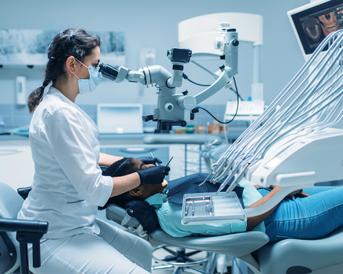 Otturazioni dentali mostra una dentista che utilizza un microscopio operatorio mentre esegue una procedura di precisione sulla paziente, necessaria per individuare e trattare carie profonde da otturare con massima accuratezza