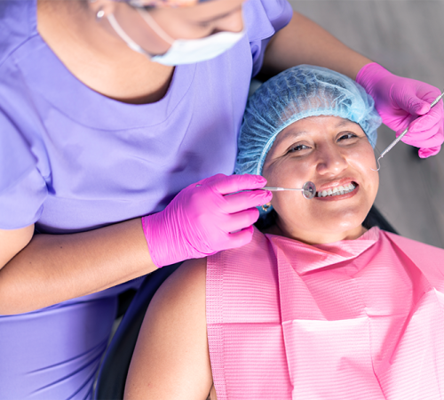 Trattamenti odontoiatrici evidenzia una paziente adulta sorridente mentre l’odontoiatra effettua un controllo orale con strumenti clinici