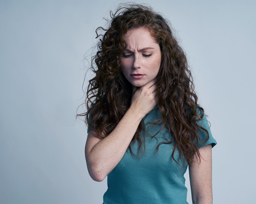 trattamenti odontoiatrici evidenzia una donna con capelli ricci che si tocca la gola mostrando un possibile disagio o dolore