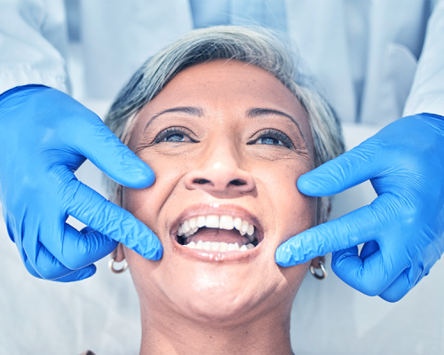 trattamenti odontoiatrici evidenzia una paziente matura che mostra il sorriso mentre il dentista indica l’area orale con guanti blu