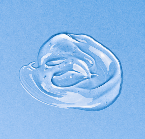 Sbiancamento dentale domiciliare mostra un gel trasparente applicato su sfondo azzurro, simbolo dei prodotti sbiancanti usati a casa, e un sorriso luminoso protetto da uno scudo grafico che rappresenta la sicurezza del trattamento.