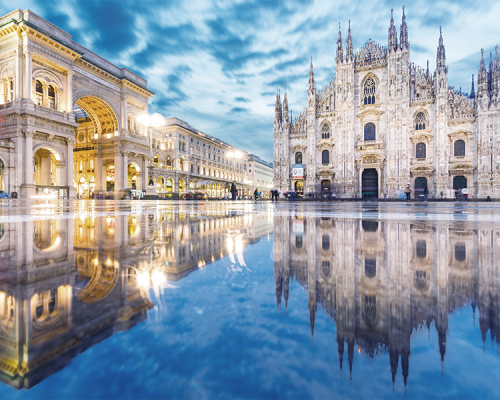Il Duomo di Milano illuminato e la Galleria Vittorio Emanuele II si riflettono in una piazza umida e lucente al tramonto, con i bambini dentali che giocano sotto un cielo nuvoloso a Milano, Italia.