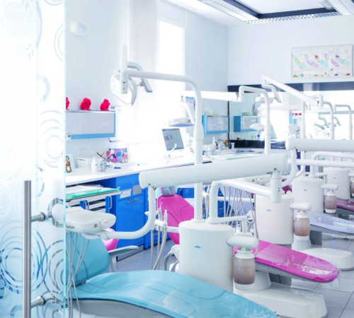 Implantologia dentale mostra uno studio dentistico luminoso e moderno, con diverse poltrone dai colori pastello, attrezzature e strumenti dentali disposti in modo ordinato; grandi finestre forniscono luce naturale.