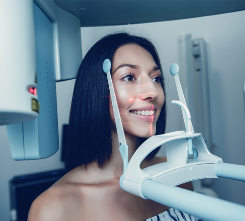 Implantologia dentale mostra Uìuna donna in piedi in una macchina per imaging dentale, con le guide di posizionamento vicino alla testa e le luci di allineamento rosse sul viso, si prepara per una radiografia dentale panoramica.