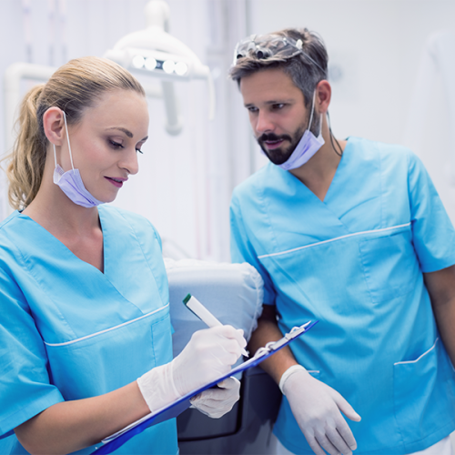 Ipomineralizzazione denti bambini rappresentata da due dentisti in divisa azzurra con mascherine abbassate e guanti, mentre consultano e compilano una cartella clinica su una clip-board all’interno di uno studio odontoiatrico luminoso.